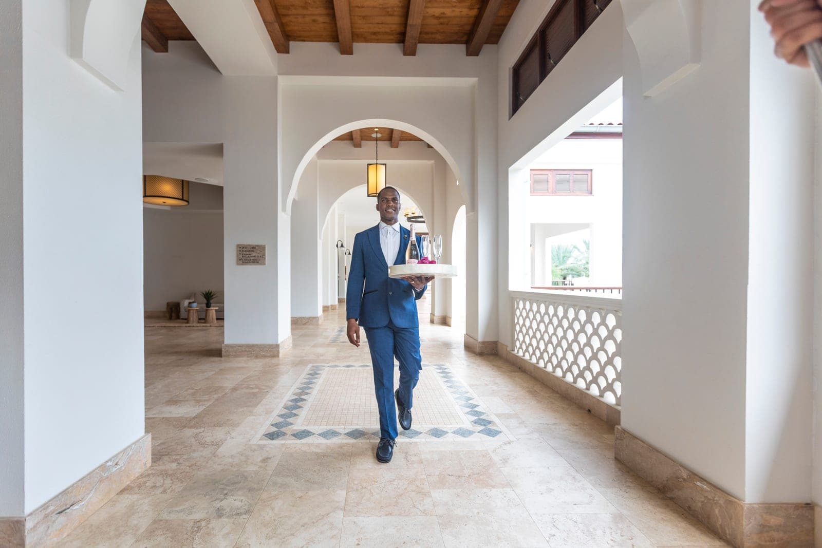 A butler carrying a champagne tray through an arched breezeway at Sandals Royal Curaçao